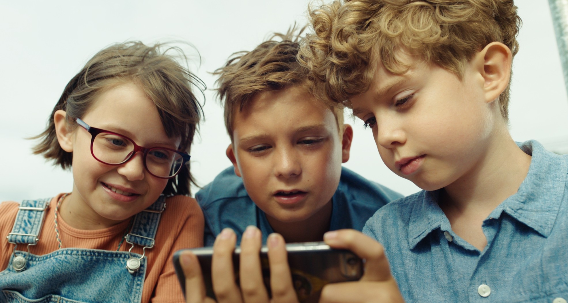 Ein  Mädchen und zwei Jungen schauen zusammen auf ein Smartphone.
