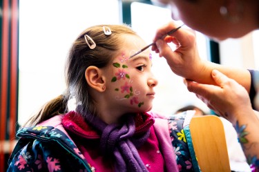Ein Mädchen bekommt Blumen ins Gesicht gemalt.